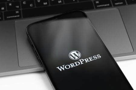 WordPress logo on screen smartphone, iPhone with notebook MacBoo